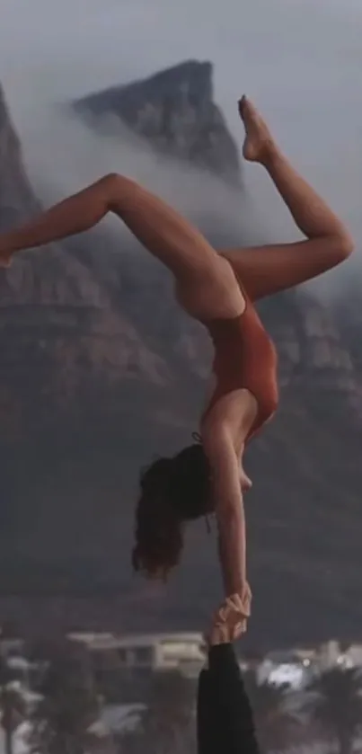 Acrobatic pose against a mountain backdrop, showcasing balance and strength.