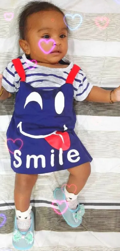 Adorable baby in blue dress on striped bedding.