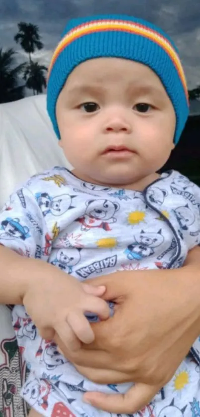 A baby wearing a blue knitted hat and patterned outfit, held in loving arms.