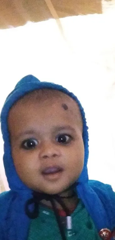 Adorable baby with big eyes in a blue hoodie mobile wallpaper.