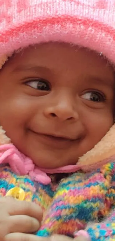 Adorable baby in colorful outfit with pink hat, smiling warmly.