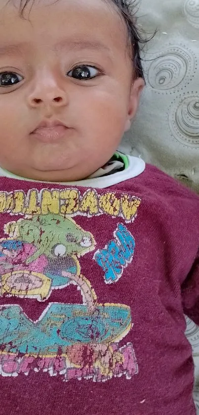 Adorable baby in maroon outfit lying down outdoors.