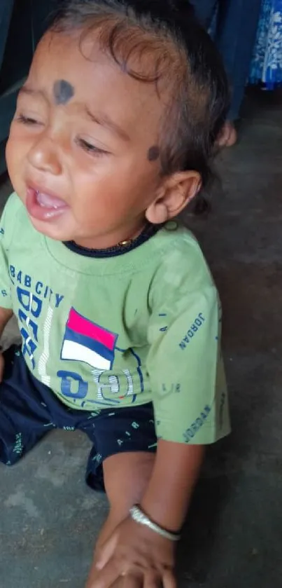 Adorable baby in a green shirt sitting indoors.