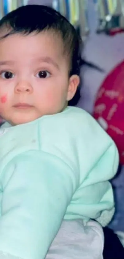 Adorable baby in mint green outfit against festive background.