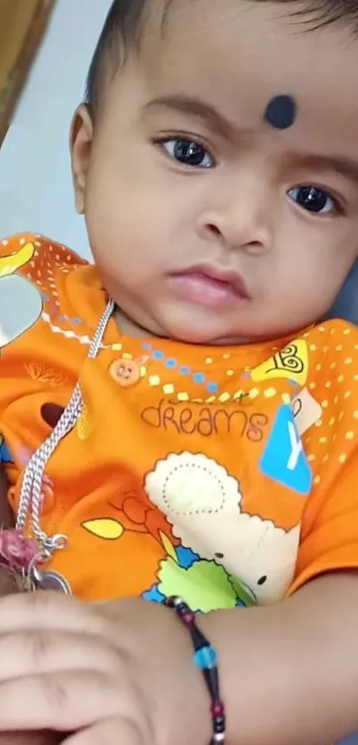 Smiling baby in orange outfit with bright colors.