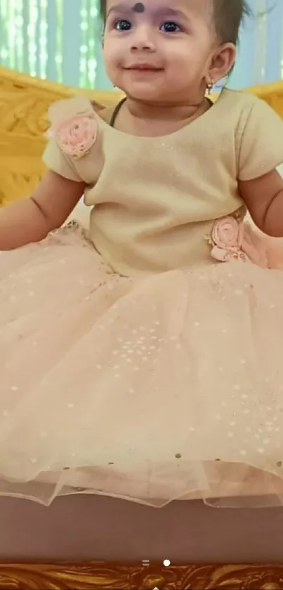 Adorable baby girl in a peachy pink dress sitting on a bed.