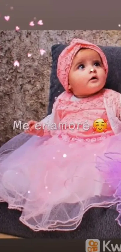 Adorable baby in pink dress with hearts, sitting on a gray sofa.