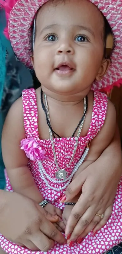 Adorable baby in pink dress and hat, smiling warmly.