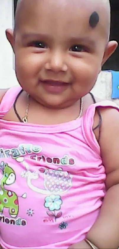 Smiling baby in pink outfit with a playful expression.