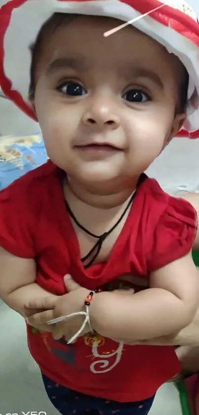 Adorable baby in red outfit and hat, smiling.