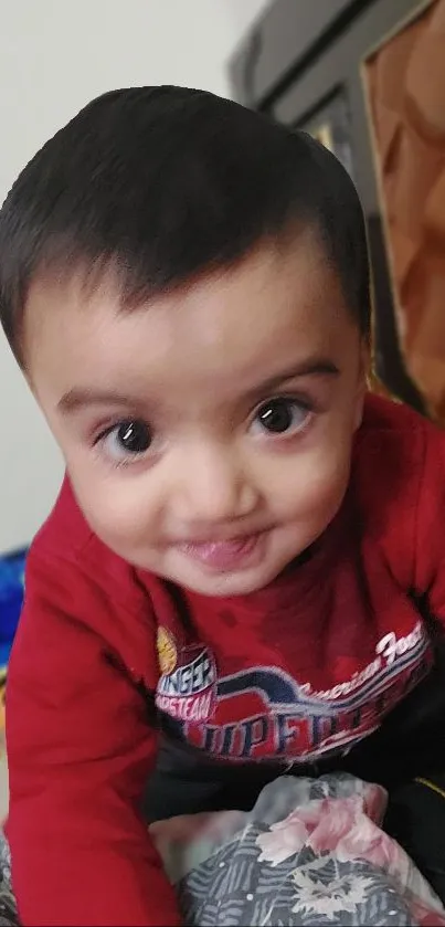 Adorable baby in red sweater smiling playfully at the camera.