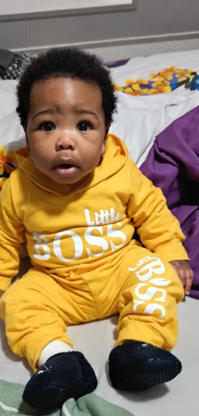 Cute baby in a yellow 'Little Boss' outfit sitting on colorful sheets.