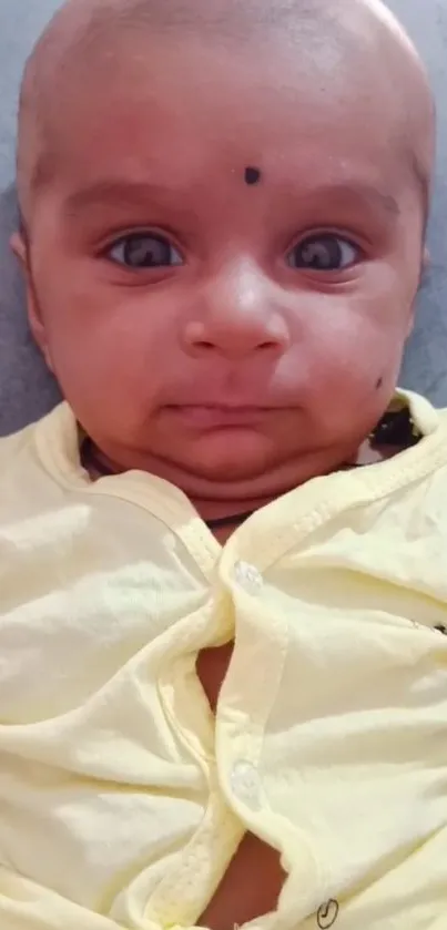 Adorable baby smiling in a yellow outfit against a soft backdrop.