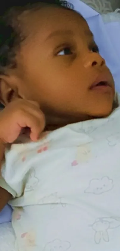 Adorable baby lying on soft bedding with a cute printed onesie.