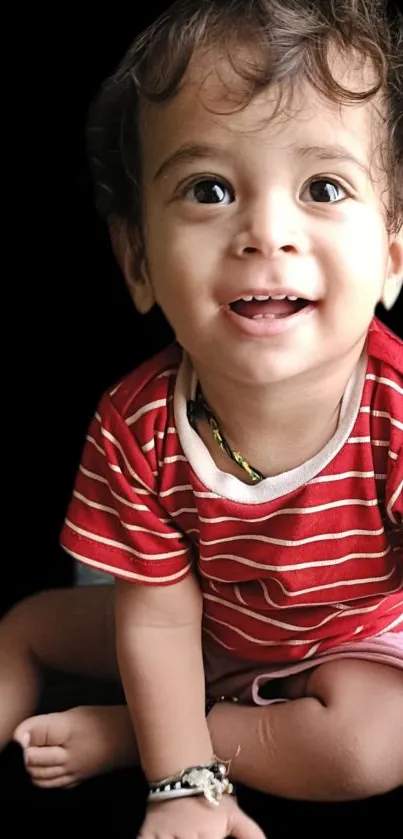 Smiling baby in red striped shirt on black background.