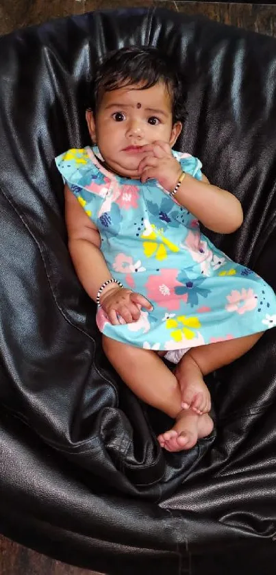 Adorable baby in a floral dress on a black bean bag.