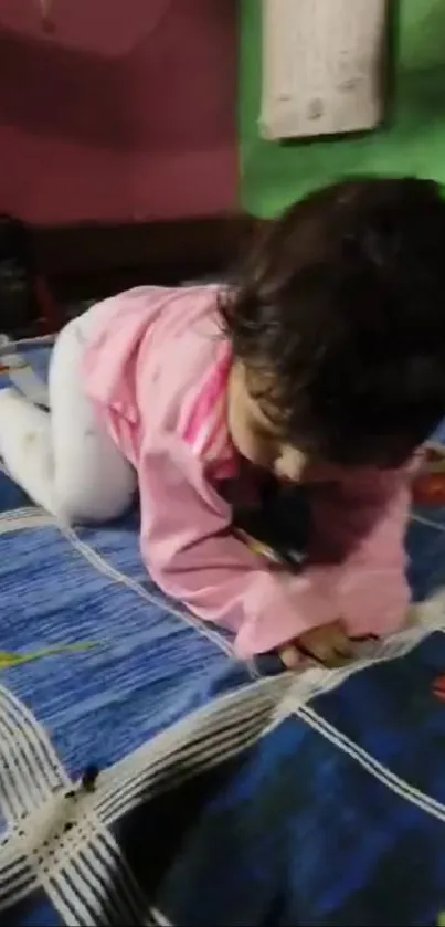 Child wearing pink pajamas on a bed with a blue cover.