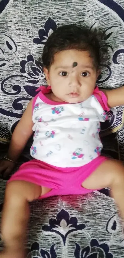 Adorable baby sitting on a decorative chair with a patterned background.