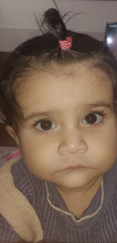 Adorable baby portrait with a small topknot, wide eyes, and neutral expression.