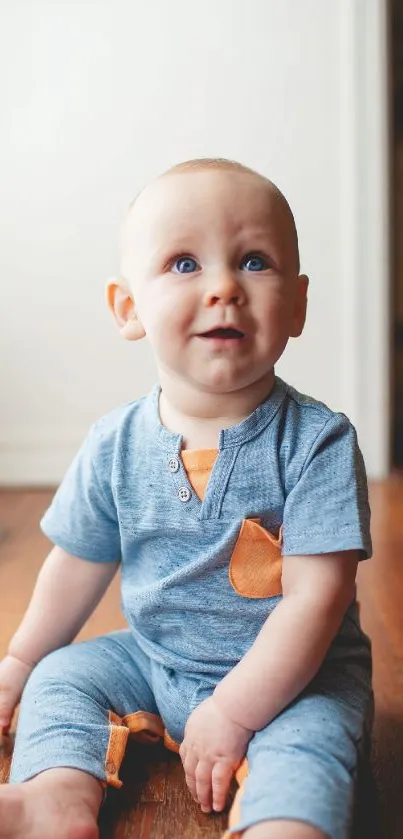 Adorable baby in blue outfit sitting on a wooden floor.