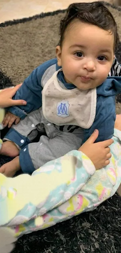 Adorable baby sitting on a dark rug, smiling gently.