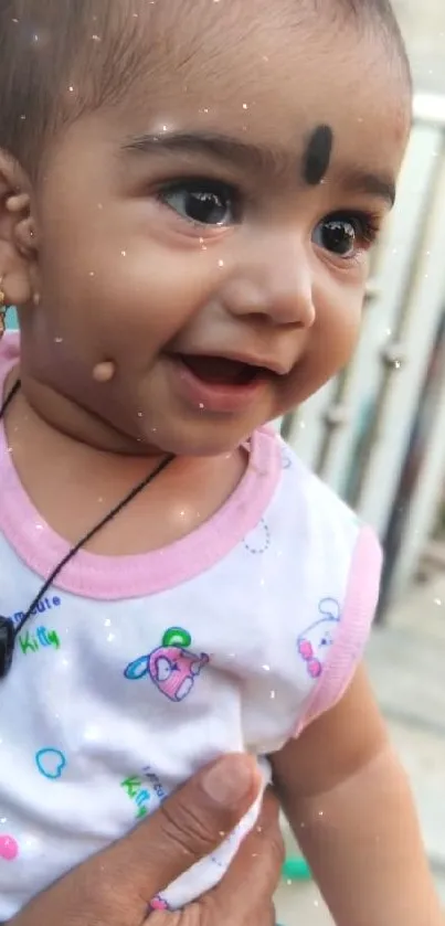 Adorable baby smiling, wearing white outfit and necklace.