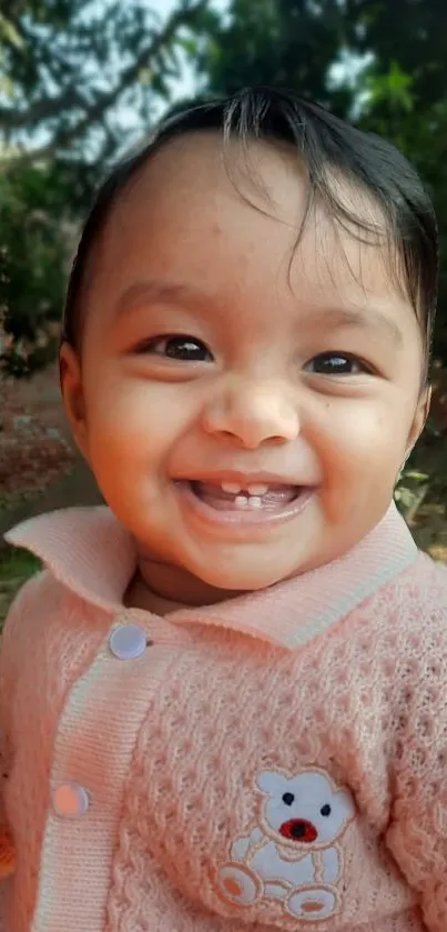 Adorable smiling baby in pink sweater with outdoor background.