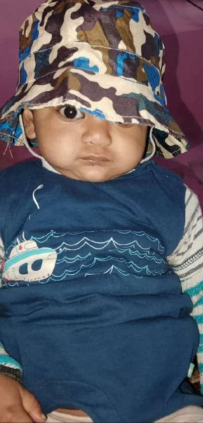 Adorable baby with a camo hat and blue outfit.