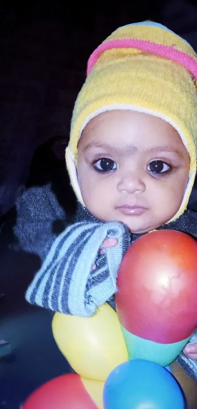 Adorable baby with colorful balloons in a cute hat.