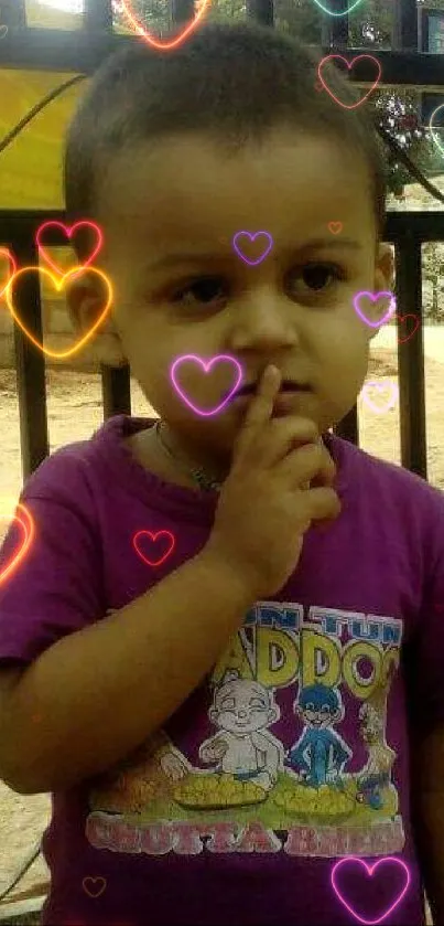 Toddler in purple shirt standing at a gate.