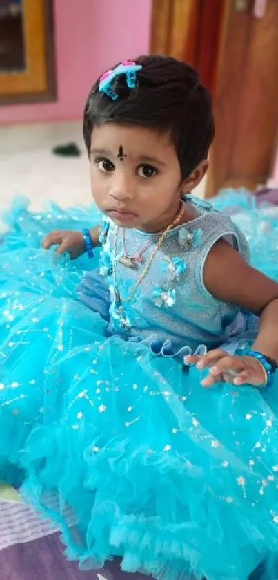 Child in a sparkling blue dress sitting indoors.