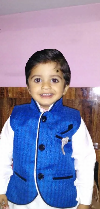 Adorable child with a bright smile in a blue outfit against a wooden background.