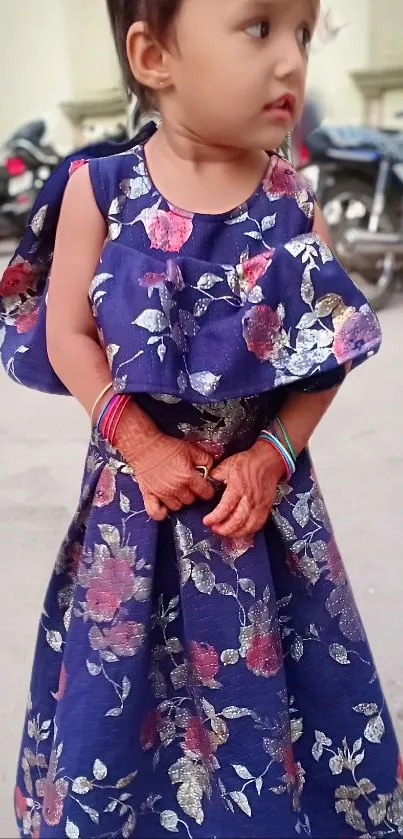 Cute child wearing a blue floral dress with bangles, standing outside.