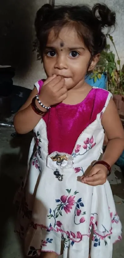 Adorable child in a floral dress standing indoors.