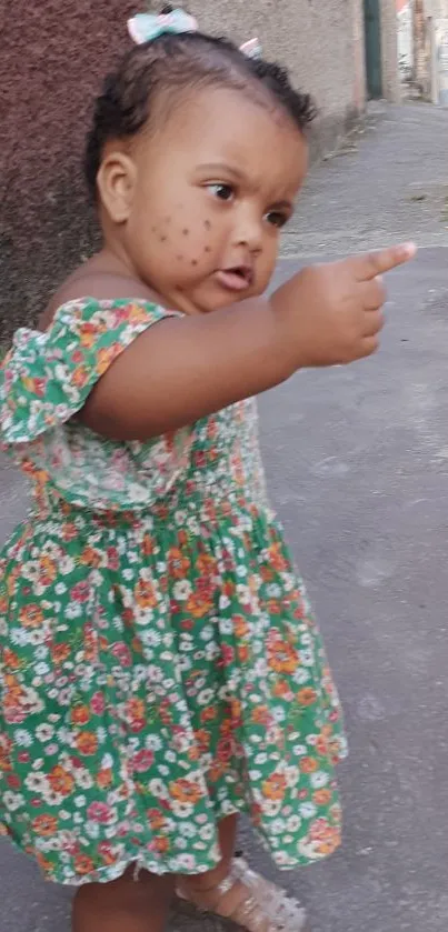 Adorable child in a floral dress pointing forward.