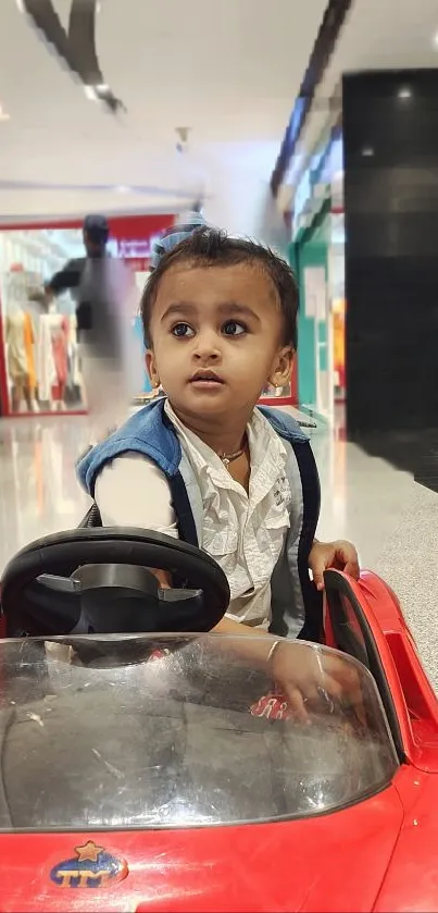 Young child driving a red toy car.