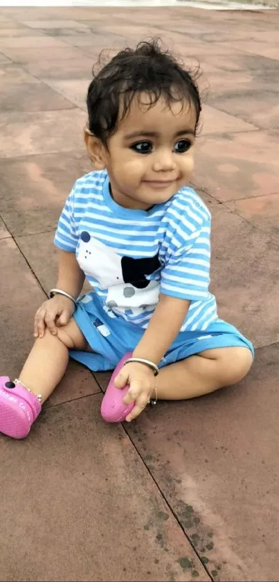 Adorable child in striped blue outfit sitting outdoors.