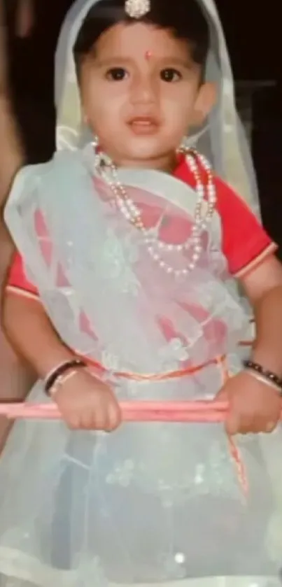 Adorable child in traditional attire holding a stick, smiling.