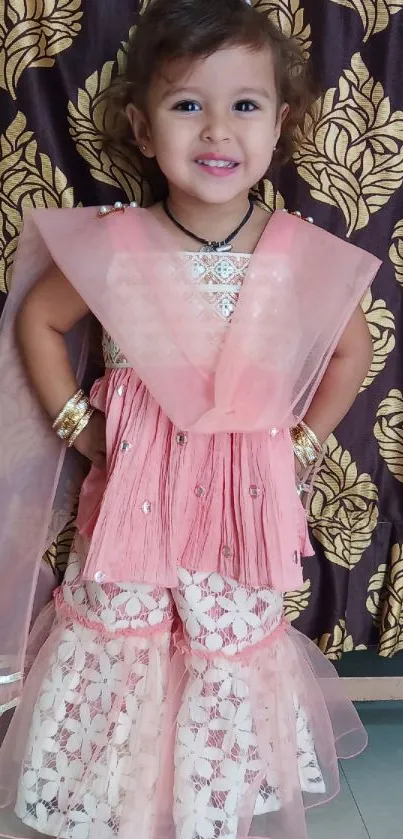 A little girl in pink traditional attire smiles brightly.