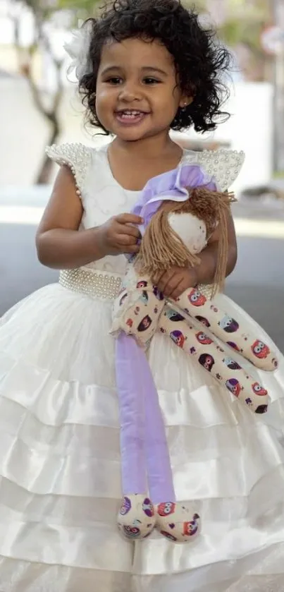 Adorable child in a white dress holding a doll outside.