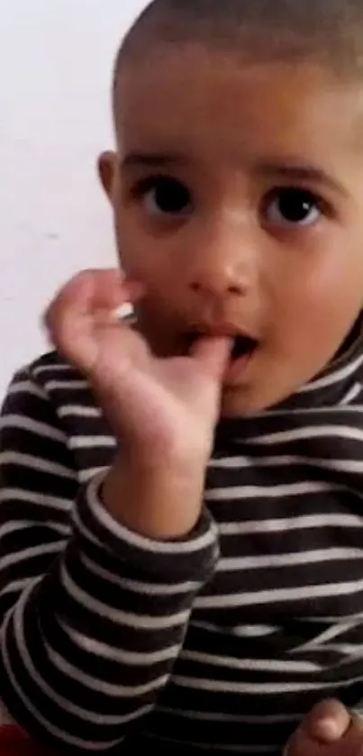 Adorable child wearing a striped shirt, sucking thumb.