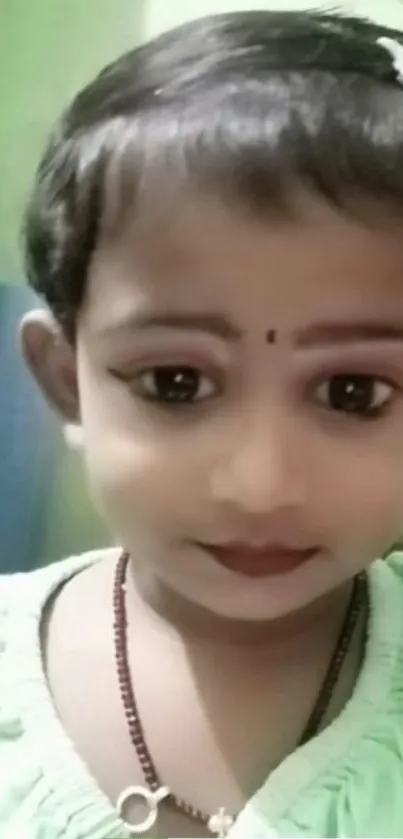 Charming child with big eyes and bindi in green attire.