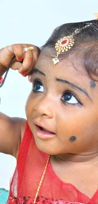 Adorable child in red attire with traditional jewelry and bright eyes.