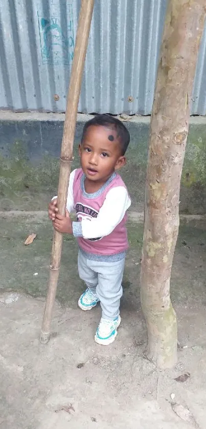 Adorable child standing with bamboo and tree in a serene outdoor setting.