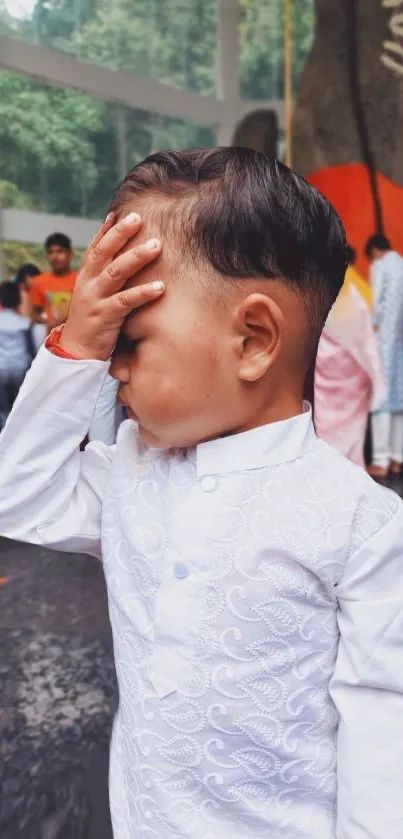 Child in white traditional attire with hand on forehead.