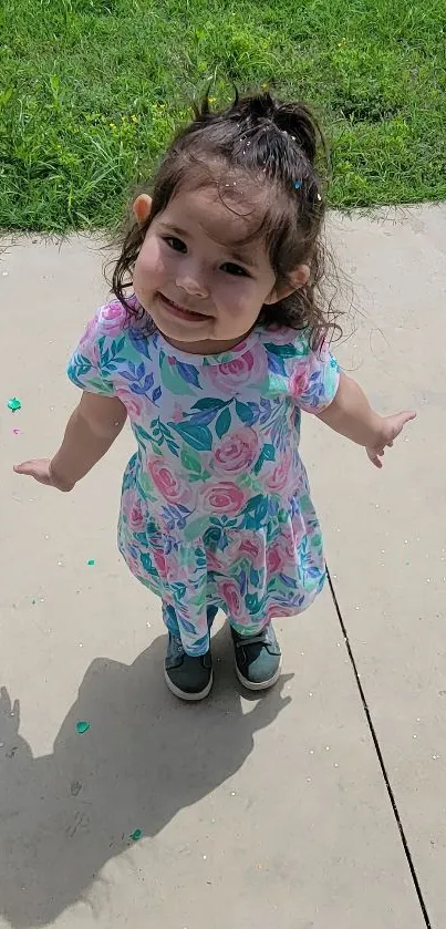 Cute child in floral dress on sunny path with grass.