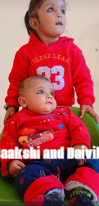 Two adorable children in red outfits, one sitting in a green seat.