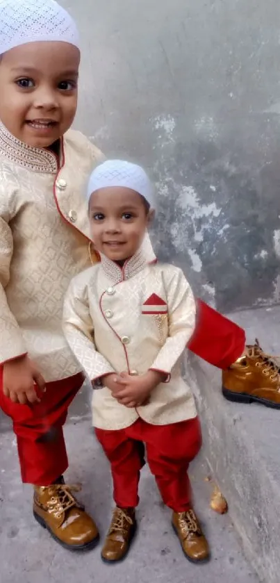 Two smiling children in traditional beige and red attire on a neutral background.