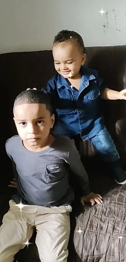 Two happy kids sitting on a dark sofa indoors.