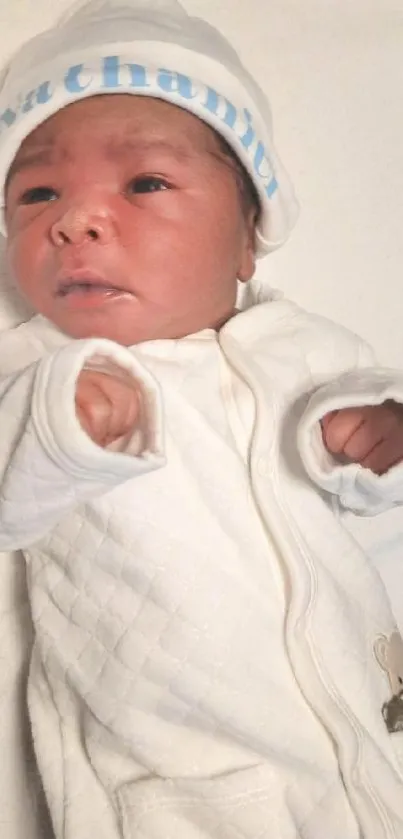 Charming newborn baby in a white onesie with matching hat on a soft background.